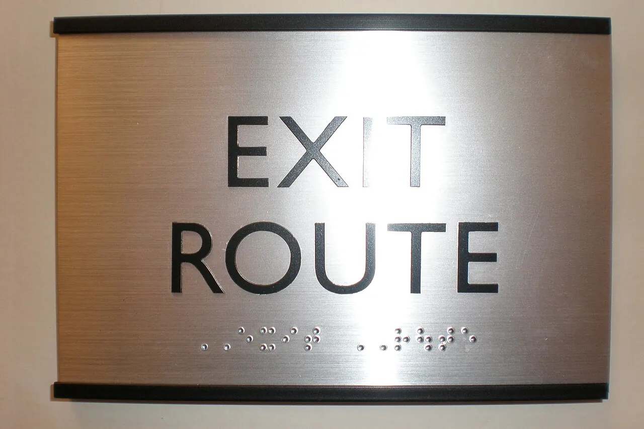 An exit route sign with braille beneath the lettering