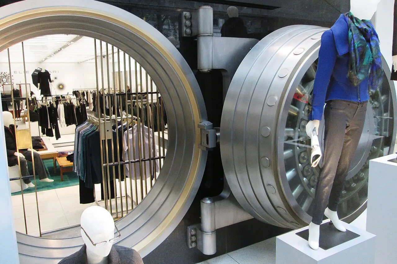 An open bank vault door with a clothing rail behind it